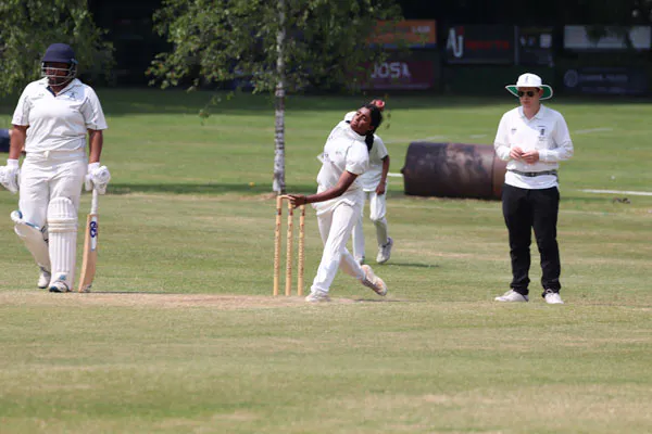 Young Women's player in her delivery stride with batter to her right and umpire behind. North London CC